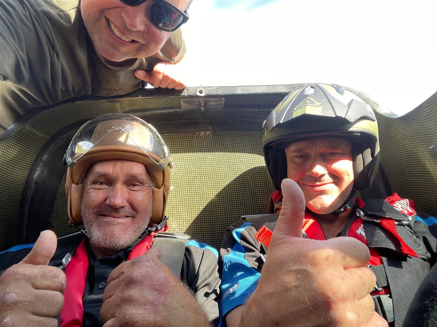 Two grinning passengers in helmets giving a thumbs up from the F1 Super Boat cockpit
