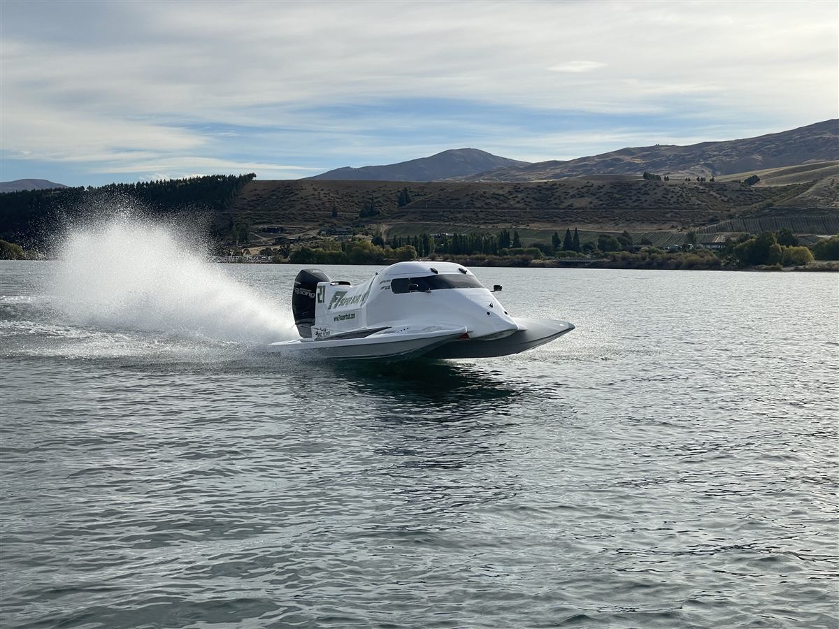 F1 Super Boat NZ speed boat throwing spray on Lake Dunstan near Cromwell, Central Otago hills behind